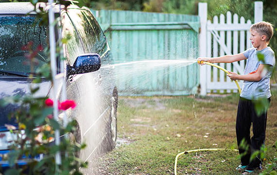 a boy sprays a car with a garden hose