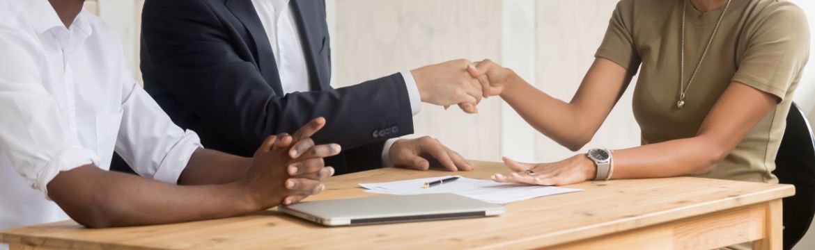 People shaking hands with laptop and papers