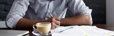 Man writing on papers with a cup of coffee in front of him